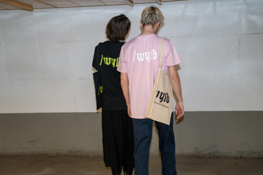Zwei Personen tragen T-Shirts mit dem wyld Logo am Rücken. Dieses Bild wird durch Anklicken geöffnet und kann dann in voller Größe gedownloadet werden.